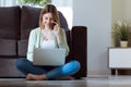 Beautiful young woman using her smartphone while working with laptop at home. Royalty Free Stock Photo