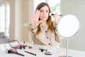 Beautiful young woman using make up cosmetics applying color using brush with open hand doing stop sign with serious and confident