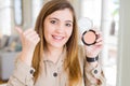 Beautiful young woman using make up cosmetics applying powder pointing and showing with thumb up to the side with happy face