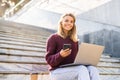 Beautiful young woman using mobile phone and laptop while sitting on a stairs Royalty Free Stock Photo