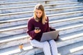 Beautiful young woman using mobile phone and laptop while sitting on a stairs Royalty Free Stock Photo