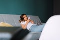Beautiful young woman using smartphone while relaxing on sofa at living room Royalty Free Stock Photo