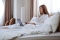 A beautiful young woman using and working on laptop computer while lying on bed at home Royalty Free Stock Photo