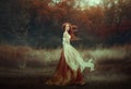 Beautiful young woman with very long red hair in a golden medieval dress walking through the autumn forest. Long red