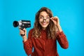 Beautiful young woman with vintage video camera on blue background
