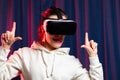A beautiful young woman in virtual reality glasses plays video games and a white hoodie on a purple background. Modern technologie Royalty Free Stock Photo