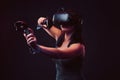 Beautiful young woman with virtual reality headset and joysticks playing video games.