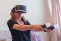 Beautiful young woman with virtual reality headset and joysticks playing video games home sitting on the sofa Royalty Free Stock Photo