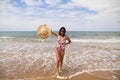 Beautiful young woman walking along the beach with a hat to protect herself from the sun. The woman is enjoying her trip to a Royalty Free Stock Photo