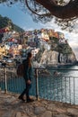 Beautiful young woman walking along the promenade of Manarola looking at stunning panoramic view of Manarola village in the Cinque