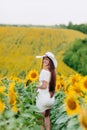 Beautiful young woman walking in blooming sunflowers field in summer. Stylish girl with long hair in white dress and hat. summer Royalty Free Stock Photo