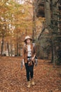 Attractive young woman in a stylish hat and travel bag on her shoulders, looking around at the charming autumn forest Royalty Free Stock Photo