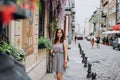 Beautiful young woman walking through the old city. Brunette girl in dress with handbag and glasses. Woman and city in summer