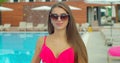 Beautiful young woman walking by the pool holding sprinkled pink inflatable flamingo float in summer. Pool summer