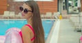 Beautiful young woman walking by the pool holding sprinkled pink inflatable flamingo float in summer. Pool summer