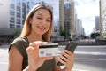 Beautiful young woman watching her credit card number using her smartphone for shopping online in finance district Royalty Free Stock Photo