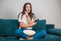 Beautiful young woman watching scary movie on the sofa eating popcorn feeling comfortable on the sofa at home looking Royalty Free Stock Photo