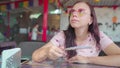 A beautiful young woman is waving a fan in the sweltering heat in a tropical cafe.