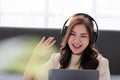 Beautiful young woman wear headphones and using laptop while sitting on sofa at home, work from home, conference meeting Royalty Free Stock Photo