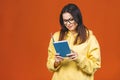 Beautiful young woman wearing casual standing isolated over orange background, reading a book Royalty Free Stock Photo