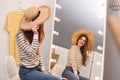 Beautiful young woman wearing hat looking at herself in mirror indoors Royalty Free Stock Photo