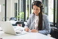 Beautiful young woman wearing headset writing notes to notebook while working in office Royalty Free Stock Photo