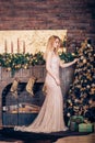 A beautiful young woman wearing a long Golden dress adorns the Christmas tree with toys and balls in the house near the fireplace Royalty Free Stock Photo