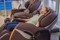 Beautiful young woman wearing a medical mask due to the coronavirus COVID 19 relaxing on the massage chair in airport or Royalty Free Stock Photo