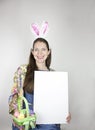 Beautiful young woman wearing rabbit ears and holding green basket with sequin Easter eggs and blank sign Royalty Free Stock Photo