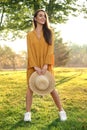 Beautiful young woman wearing stylish yellow dress with straw hat in park Royalty Free Stock Photo