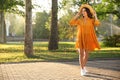 Beautiful young woman wearing stylish yellow dress and straw hat in park Royalty Free Stock Photo