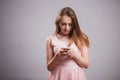 Beautiful young woman wears pink dress and uses smartphone on grey background with copy space