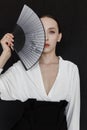 Beautiful young woman in a white Asian suit on a black background. The style of a modern geisha in the studio.