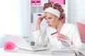 Beautiful young woman in white bathrobe sitting at table with laptop Royalty Free Stock Photo