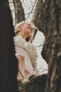 A beautiful young woman in a white chiffon dress with a short blonde haircut is sitting on a tree, bottom view Royalty Free Stock Photo