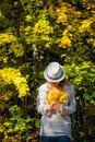 Beautiful young woman in white clothes and hat tilted her head to the bouquet of yellow leaves in her hands. Elegant blonde, face