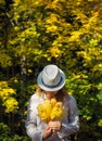 Beautiful young woman in white clothes and hat tilted her head to the bouquet of yellow leaves in her hands. Elegant blonde, face