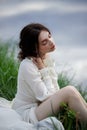 Beautiful young woman in white dress resting on shore lake pond river. Professional makeup and hairstyle with curled hair Royalty Free Stock Photo