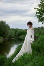 Beautiful young woman in white dress resting on shore lake pond river. Professional makeup and hairstyle with curled hair Royalty Free Stock Photo