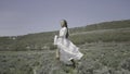 Beautiful young woman in white dress runs into field. Action. Attractive woman in white dress runs across green field on Royalty Free Stock Photo