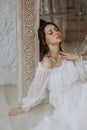 A beautiful young woman in a white dress sits on the sand next to a mirror and touches her neck Royalty Free Stock Photo