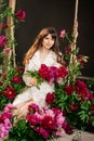 a beautiful young woman in a white dress sits on a swing in peony flowers. Royalty Free Stock Photo