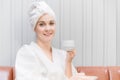 Beautiful young woman in white dress sitting on couch and smile with holding coffee cup and drinking in spa salon Royalty Free Stock Photo