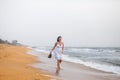 Beautiful young woman in white dress walking on the sandy beach, holding sandals. travel and Summer concept Royalty Free Stock Photo