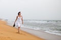 Beautiful young woman in white dress walking on the sandy beach, holding sandals. travel and Summer concept Royalty Free Stock Photo