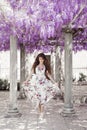 Beautiful young woman in white flying dress over wisteria tunnel