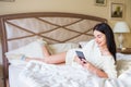 Beautiful young woman in white knitted dress reading text message on her mobile phone and smiling. Royalty Free Stock Photo