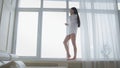 Beautiful young woman in a white men`s shirt and socks walking on windowsill, laughing and talking on the phone happily Royalty Free Stock Photo