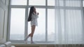 Beautiful young woman in a white men`s shirt and socks walking on windowsill, laughing and talking on the phone happily Royalty Free Stock Photo