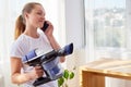 Beautiful young woman in white shirt holding vacuum cleaner and talking on cellphone, copy space. Housework, spring-cleanig.